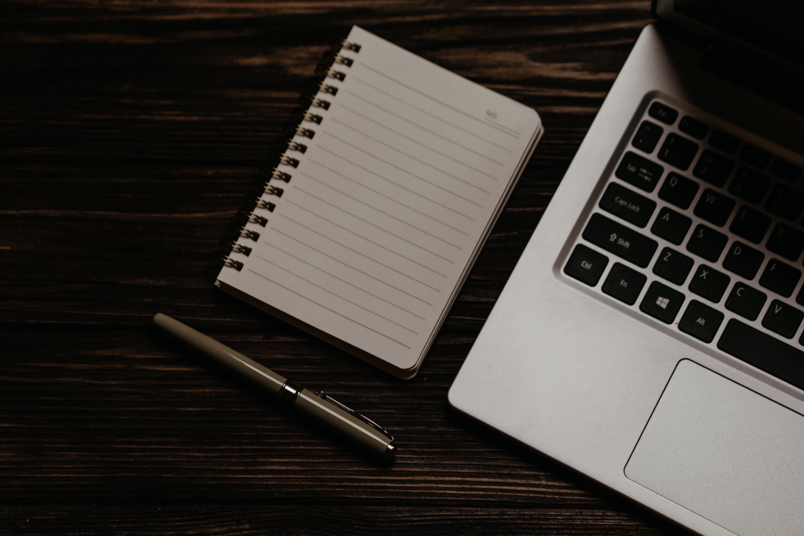 A notebook and laptop arranged on a dark wooden desk